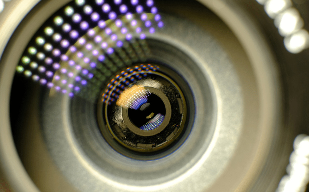 Close-up of a camera lens showing detailed reflections and colored dots, with intricate textures in the components—capturing clarity similar to what you experience when you request a demo to see Radiant Logic in action.