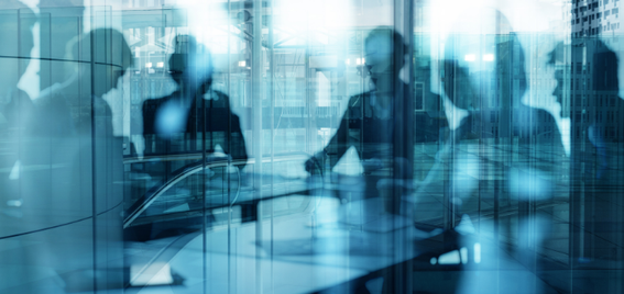 Silhouettes of people having a meeting around a table in a modern glass office, with reflections and city buildings visible through the windows.