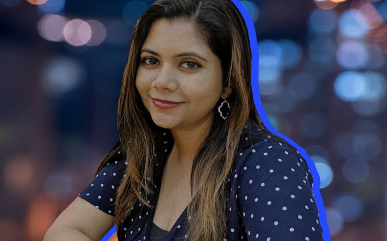 A woman with long brown hair and a polka-dot top smiles softly at the camera; the background is blurred with blue and orange lights, and a blue outline highlights her silhouette.