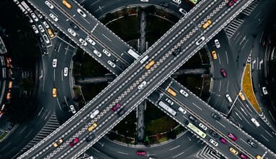 Aerial view of a busy multi-level highway interchange with intersecting roads, roundabouts, and numerous cars and taxis traveling in various directions.