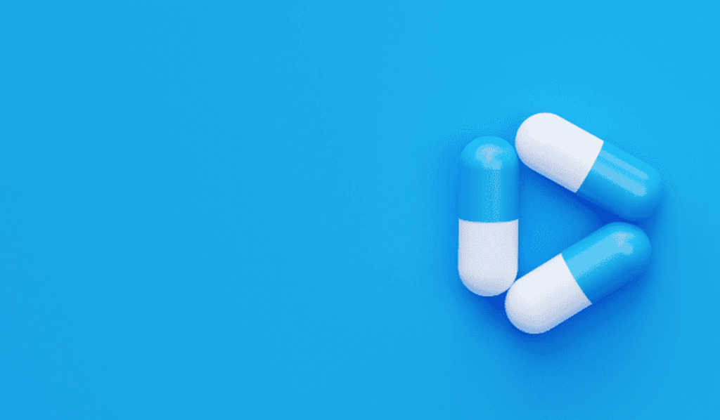 Three blue and white capsules are arranged in a triangular shape on a bright blue background, with ample empty space on the left side.