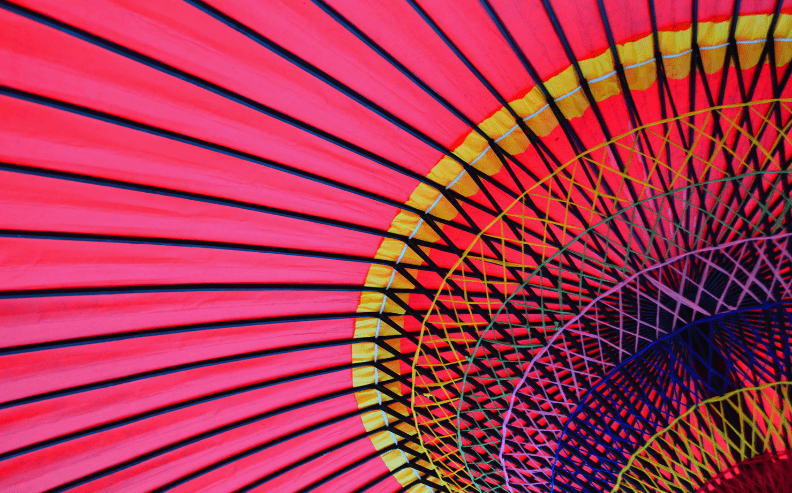 Close-up view of the vibrant, colorful underside of a traditional paper umbrella, displaying radiating lines and patterns in red, yellow, blue, and black.
