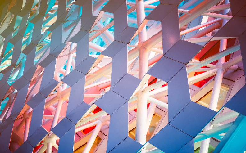 Geometric architectural structure with interlocking hexagonal panels and crisscrossing white beams, illuminated by colorful pink, blue, and orange lights.