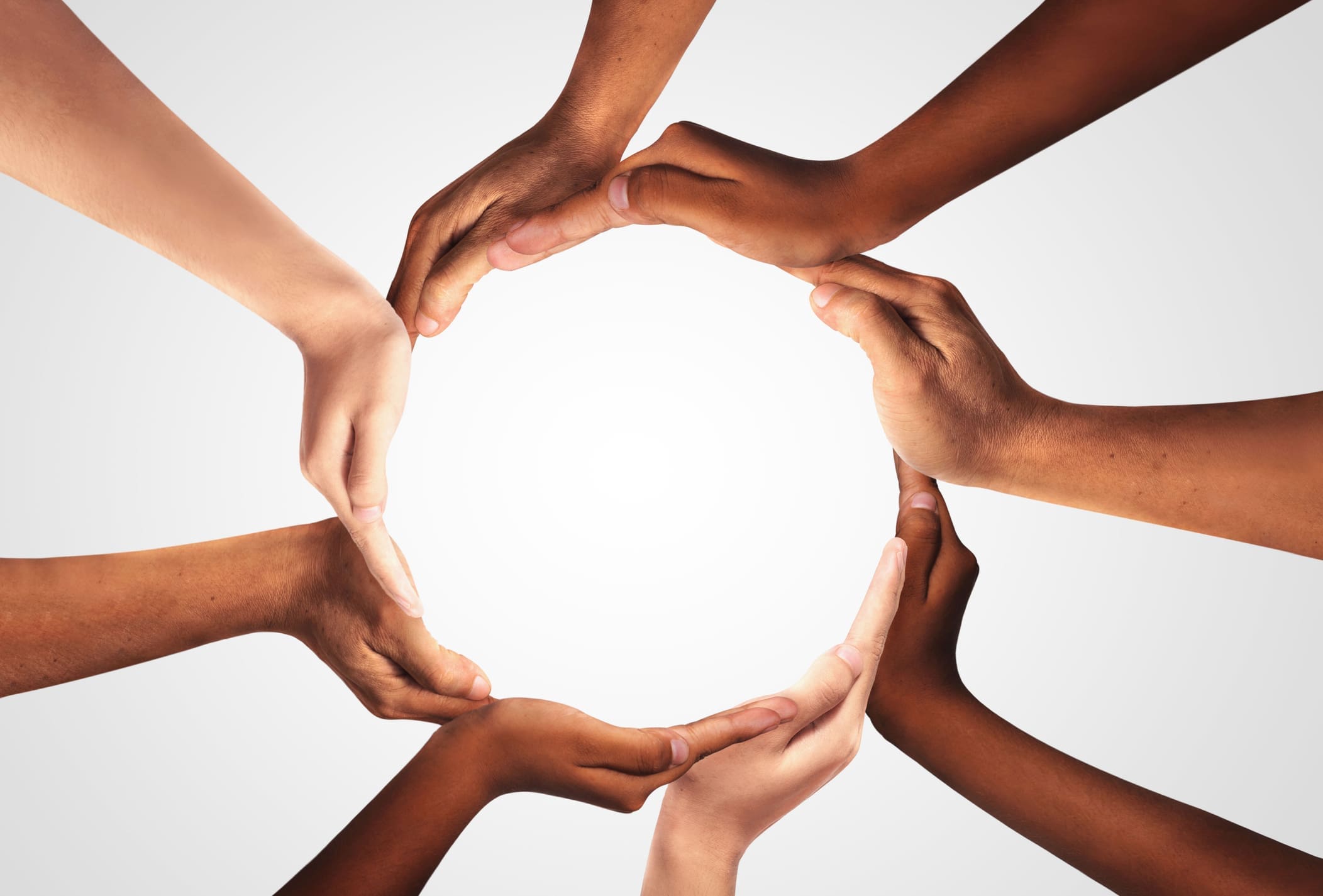 A diverse group of hands with different skin tones form a circular shape against a white background, symbolizing unity and teamwork.